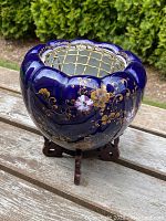 Front angled view of the powder blue Chinese bowl on wooden stand, showing gold gilt floral decoration and metal lattice insert.
