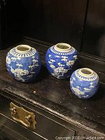 Three antique Chinese blue and white ginger jars displayed together on a dark surface, showing different sizes and floral designs.