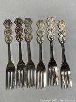 Six antique Chinese silver forks laid side by side showing decorative tops with Chinese characters and three-pronged forks, displaying surface wear and tarnish.