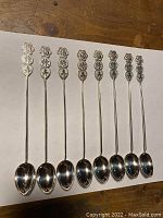 Full view of all 8 antique Chinese silver long spoons laid side by side showing the detailed handles and spoon bowls.