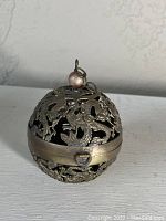 Photo of antique spherical metal incense burner with open dragon carvings and tarnishing, showing front view with hanging ring and bead on top