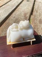 Front three-quarter view of white jade Foo Lion on ivory-tone platform and hardwood stand