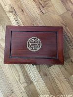 Top view of rectangular red wood jewelry box showing circular metal plaque with Chinese symbol in center.