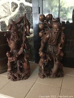 Front view of two wood carvings side by side on tile surface with stone background.