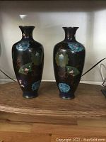 Pair of tall antique Japanese cloisonne vases displayed side by side on a wooden surface, showing overall design and size comparison.