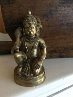 Front view of metal kneeling Buddha figure showing detailed facial features, headdress, and mace in right hand.