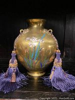 Front view showing overall vase shape, enamel floral detail, and purple silk tassels on handles.
