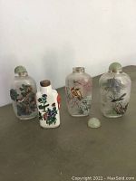 Four Chinese snuff bottles displayed in a row on a surface, showing various hand-painted inside decorations and some lids removed or seized.