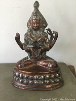 Front view of antique Buddha figure showing detailed face, multiple arms, copper body and silver base.