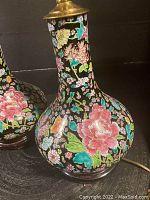 Close-up of one lamp’s black-ground porcelain body showing hand-painted polychrome floral decoration.