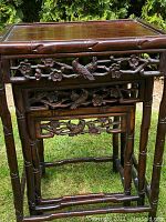 Three nested hardwood tables of varying heights with carved aprons and bamboo-style legs