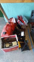 Overview of automotive items on floor including red gas containers, jack stands, car stereo and other parts.