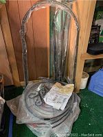 Photo of the black round bakers rack metal parts bundled together in plastic wrapping, includes tubular sections and arch top.