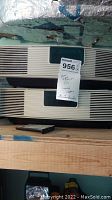 Two stacked Bose Wave Radio units with a sticky note and the remote control in front, showing general condition and size.