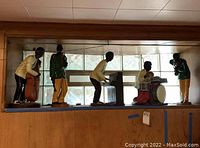 Wide view showing all six ceramic jazz musicians and the piano figurine arranged on a shelf against a window and wooden paneling.