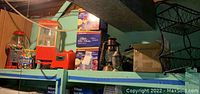 Shelf displaying gum ball machine with colored gum balls, plastic tub of Bubble Bubble gumballs, vintage lanterns, boxed apple peelers, and other decorative items