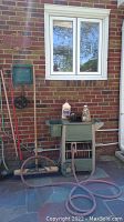 Wide view of hose reel, broom handles, dust pan, and tiki fuel on top of hose reel.
