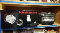 Shelf photo showing boxed KitchenAid food processor and unboxed Cook's Essentials pressure cooker side by side