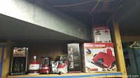 Wide view of the kitchen appliances lot on shelf showing coffee maker, mixers, choppers, and grills in original boxes