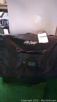 Closed black carry case with Life Gear logo embroidered, designed to hold the folding massage table, with handles and a tag attached.