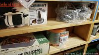 Photo showing Cuisinart Mini-Prep Plus food processor box, Meyer Professional Roaster box, and assorted pots with lids on wooden shelf.