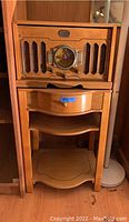 Front view of Thomas retro stereo console sitting on top of matching wood table with drawer and shelves, showing stereo details and drawer knob.