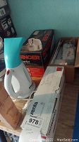 Photo of a Rowenta steam brush in white and turquoise, Singer Starlet portable sewing machine box, and boxed item on wooden surface