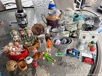 Wide view of all items arranged on glass table showing variety of antique and vintage miniatures mainly dolls, ceramic items, and small furniture.