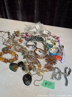 Overview of lot showing assortment of costume jewellery including beaded necklaces, several bracelets, large crystal bow-shaped brooch, and metal bangles scattered on a surface.