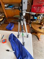 Slik 35D tripod mounted on table, showing handle, leg structure and blue carry bag on table.