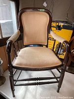 Front view of a dark wood Victorian armchair with beige fabric upholstery and carved legs.