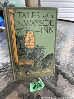Green hardcover book titled 'Tales of a Wayside Inn' by Henry Wadsworth Longfellow with illustrated inn sign on front cover.