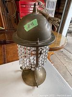 Antique solid brass table lamp with dome brass top and hanging crystal droplets, cord attached, shown on garage floor surface.