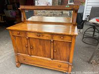 Full view of antique solid wood sideboard with mirror, showing upper drawers, three cabinet doors, large bottom drawer, and the mirror framed in wood.