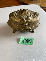Closed view of the antique Art Nouveau metal trinket vanity box showing detailed floral relief design and feet.