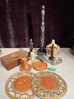 Overview of many indigenous items on display including wooden carvings, woven coasters, a basket, a carved stone bird, a small animal figurine, a wooden box, and a cone-shaped leather item.