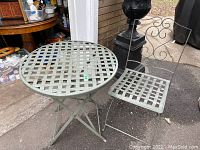 Front view of the round table and folding chair side by side outdoors on pavement showing lattice pattern and foldable design.