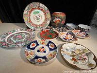 Wide view displaying the majority of the lot including the Imari plate, Fritz & Floyd jar, various plates and bowls with floral and Asian themed designs.