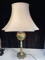 Full view of the tall solid brass converted oil lamp with white fabric shade, showing ornate base and shaft with twisted design.