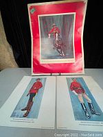 Full view of the three prints, two smaller and one larger with red border, displayed on table.