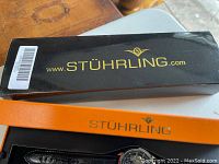 Closed black and gold Stuhrling presentation box with website logo on lid.