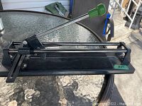 Photo showing the entire tile cutter on glass table with metal rails and green handle