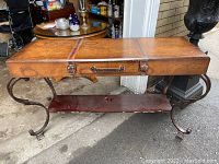 Front view of the vintage console table showing wooden top with antique map design, wrought iron legs, and lower shelf.