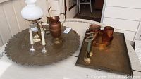Overall view of brass and copper items including lamps, trays, candlesticks, and a pitcher on a table