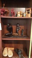 Shelf with carved African wooden man and woman kneeling figurines, small black bust, and a long wooden spear-like ornament