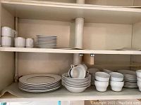 Shelves with stacked plates, bowls, and cups showing part of the Barretts Staffordshire dish set and the SK demitasse cups and saucers
