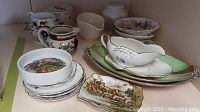 Various small china plates stacked, showing fruit design plates, gravy boat, and cream and sugar containers with floral and fruit patterns.