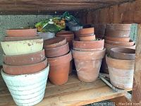 Stacked terracotta and white clay pots with some bags and items behind them