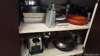 Cupboard shelf showing various cookware and kitchen items including the orange Belgium frying pan, toaster, and more.