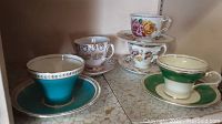 Five cups and saucers arranged on a shelf, showcasing various styles and colors: turquoise, green, floral patterns
